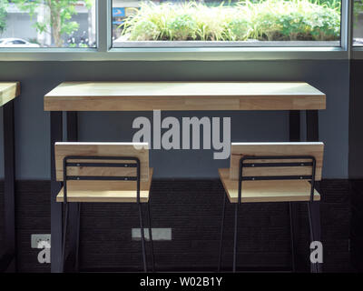 Wooden bar stools and wooden table near the window glass with morning sunshine from outside. Stock Photo