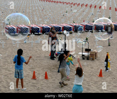 Youngsters frolic as they chase bubbles near flag-draped caskets on display at the Arlington West Memorial Project  in Santa Monica, California on May 26, 2007. The beach memorial features thousands of crosses representing the 3,452 soldiers who have died in Iraq. (UPI Photo/Jim Ruymen) Stock Photo