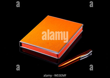 notebook and pen bright orange on a black background. Stock Photo