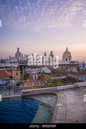 The sun sets over the rooftops and skyline of Cartagena, Colombia - view from the rooftop pool and bar of one of the center's many luxury hotels. Stock Photo
