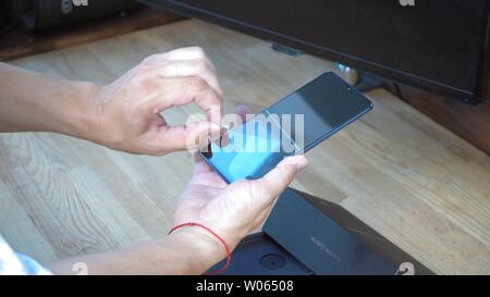 Man is holding Huawei Mate 20 X smartphone in one hand and taking off protective tape from its large and shining display. Under his hands lies opened Stock Photo