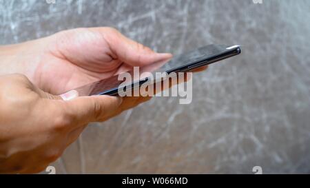 Man is holding extremey thin Huawei Mate 20 X smartphone in his both hands on shining grey background. Unlocking and volume switchers are seen on phon Stock Photo