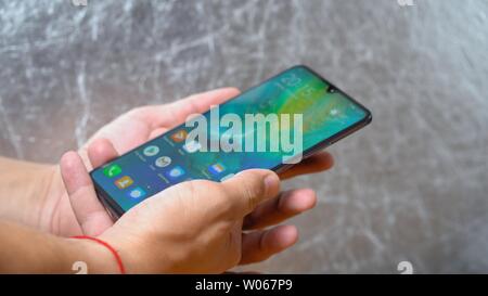 Man holding Huawei Mate 20 X smartphone with both hands on shining grey background. Display is turned on and main menu is seen Kyiv, Ukraine 15th of J Stock Photo