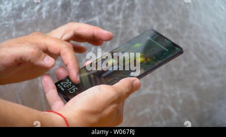 Man holding Huawei Mate 20 X smartphone in one hand and unblocking it with finger on shining grey background. Display is turned on and locker image is Stock Photo