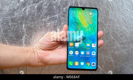 Man holding Huawei Mate 20 X smartphone in one hand on shining grey background. Display is turned on and main menu is seen Kyiv, Ukraine 15th of June Stock Photo