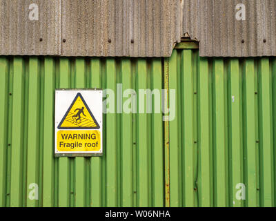 Fragile roof warning sign on side of a shed with broken wall panel for health and safety purposes Stock Photo