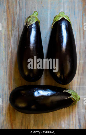 Three eggplants on a rustic wooden surface. Stock Photo