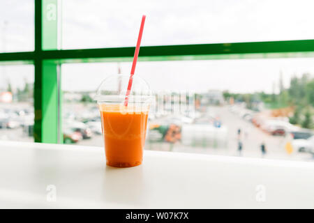 Bright orange carrot tangerine smoothie in a plastic glass with Stock Photo