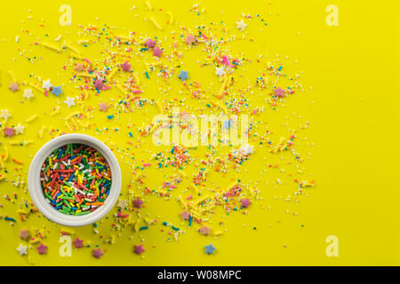 Sprinkles on bright yellow background with little white bowl with various type of coloured sprinkles at bottom  and multi-colored cake topping sprinkl Stock Photo