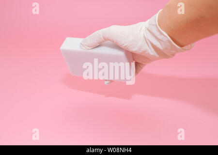 Human hand in white glove holds a white melamine household sponge for cleaning on pink background. Cleaning concept Stock Photo