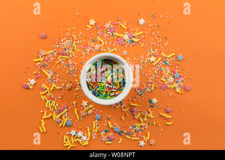Sprinkles on orange background with single little white bowl with multi-colored sprinkles in centre - top view Stock Photo