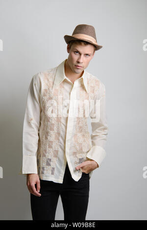 a handsome brown hair caucasian male model poses in a cream vintage 70s embroidered shirt he wears a brown fedora hat w09b8e