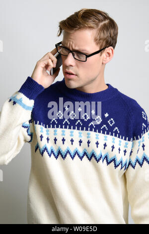 A Brown hair Caucasian male model poses in vintage sweater, wearing eyeglasses, talking on the phone. Stock Photo