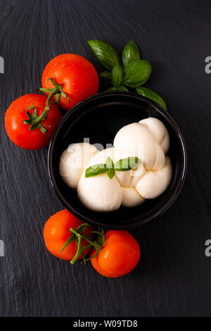 Food ingredient concept organic mozzarella cheese in black ceramic cup with  tomatoes and basil with copy space Stock Photo