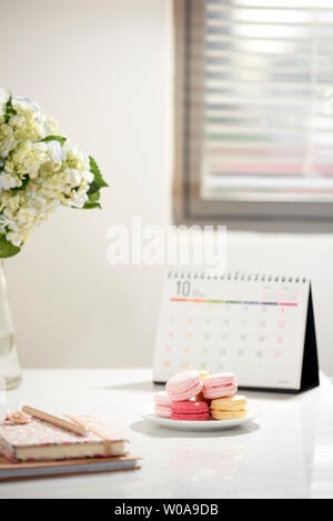 Office table desk. Feminine desk workspace frame with calendar, diary, hortensia bouquet and macaron on white background. ideas, notes or plan writing Stock Photo