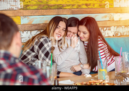 Friends comforting and consoling crying young woman at group meeting in modern pub Stock Photo