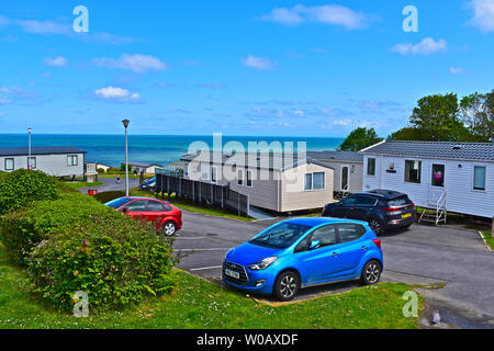 A view of static holiday caravans which overlook Cardigan Bay near Newquay in West Wales.Blue skies & white clouds. Cars parked nearby. Stock Photo
