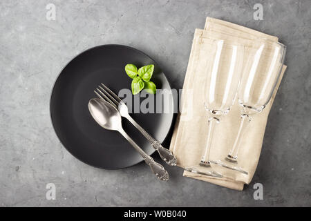 Table setting with black matte plate, wine glass and cutlery. View from above over gray concrete background. Stock Photo