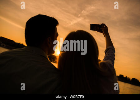 Happy couple is taking selfie in sunset in the city. Stock Photo