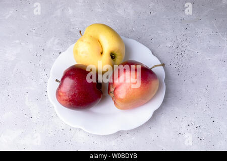 Three ugly apples on white  figured plate on grey concrete background. Stock Photo