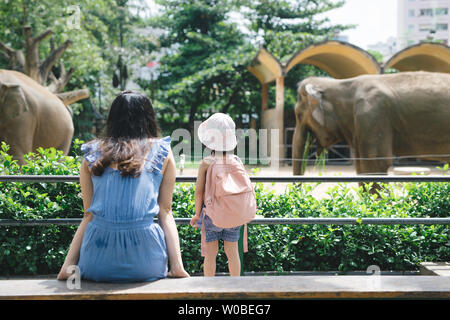 Happy mother and daughter watching and feeding elephants in zoo. Stock Photo