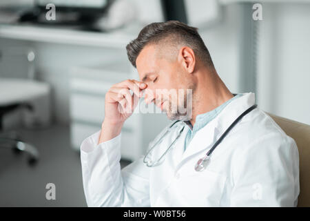 Plastic surgeon wearing white lab coat feeling sleepy and tired Stock Photo