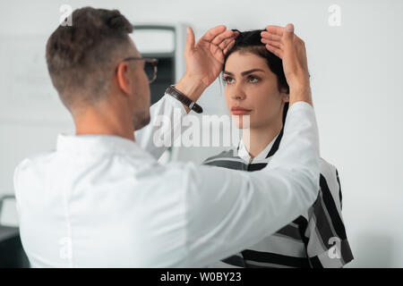 Plastic surgeon wearing glasses examining face of client Stock Photo