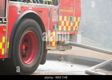 A New South Wales Fire and Rescue truck with fire hoses connected, parked in a smoke filled suburban street during a Hazard Reduction burn in Sydney Stock Photo