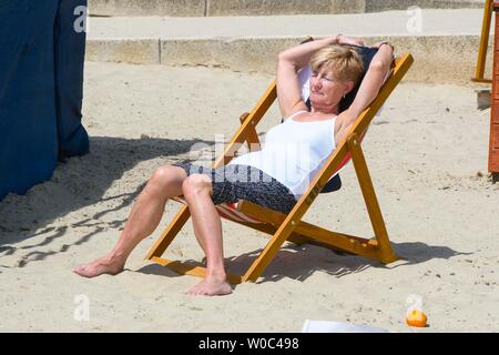 Lyme Regis, Dorset, UK.  27th June 2019. UK Weather.  A woman sunbathing at the seaside resort of Lyme Regis in Dorset as they enjoy a day of clear blue skies and scorching sunshine.   Picture Credit: Graham Hunt/Alamy Live News Stock Photo