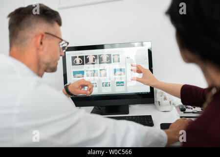 Plastic surgeon wearing glasses consulting client near computer Stock Photo