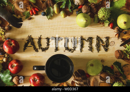 Autumn concept. A black cup of tea on a wooden table with a frame of autumn crops and falling leaves. Stock Photo
