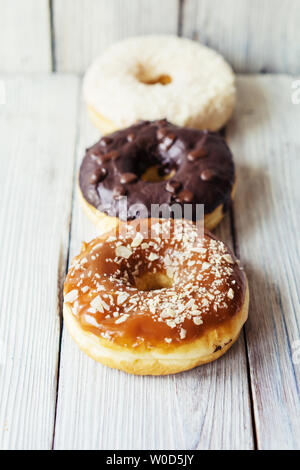 Three delicious glazed creme donuts with a scattering on a wooden background lie in a row with a retreating perspective. Pastry and fresh pastries. Stock Photo
