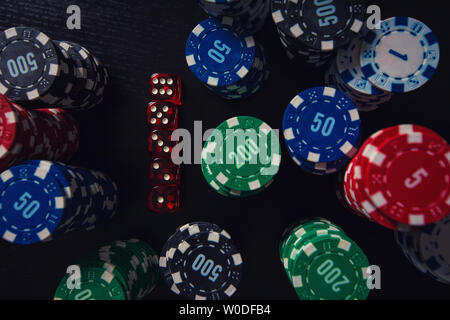 Close up stacks of different colored poker chips and playing dices on the casino table isolated over black background. Gambling tournament betting for Stock Photo
