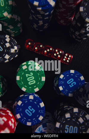 Close up stacks of different colored poker chips and playing dices on the casino table isolated over black background. Gambling tournament betting for Stock Photo