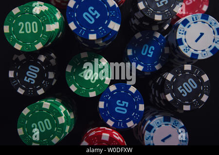 Close up stack of different colored poker chips of diverse value isolated on the black casino table background. Gambling tournament betting for succes Stock Photo