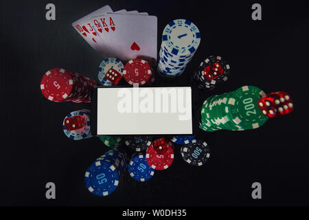 Online casino gambling concept. Smartphone blank screen on chips stack, royal flush poker cards combination and red dices over black table background. Stock Photo