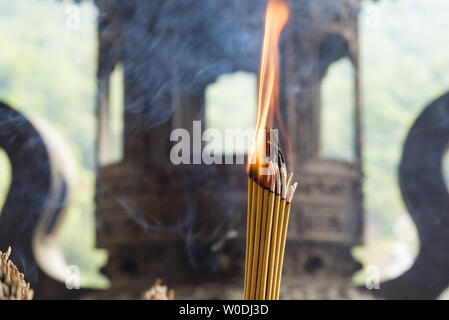 Burning incense sticks with out of focus Buddhist temple in the background. Stock Photo
