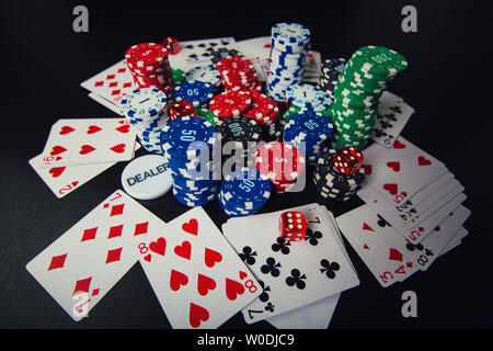 Close up stack of different colored poker chips, playing cards and dices isolated over black casino table background. Gambling tournament earnings, be Stock Photo