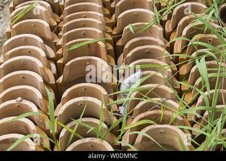 Stacks of yellow ceramic glazed curved roof tiles in a symmetrical pattern. Stock Photo