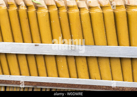 Stacks of yellow ceramic glazed curved roof tiles in a symmetrical pattern. Stock Photo