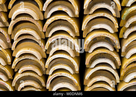 Stacks of yellow ceramic glazed curved roof tiles in a symmetrical pattern. Stock Photo