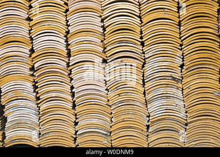 Stacks of yellow ceramic glazed curved roof tiles in a symmetrical pattern. Stock Photo