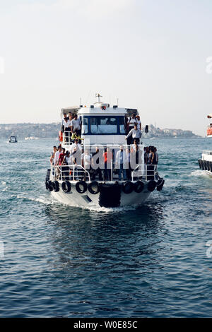 A little ferry boat prepares to moor on the riverbank of the Bosphorus with a dozen people waiting to disembark in Istanbul, Turkey Stock Photo