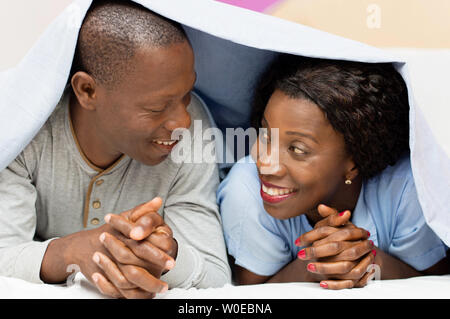 young couple lying under the cover looks, smiling. Stock Photo