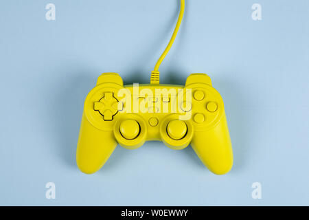 a yellow painted video game controller on a plain blue background. Minimal color still life photography Stock Photo