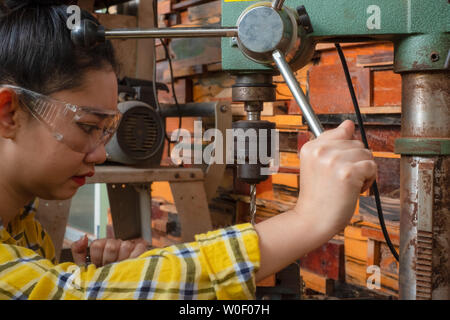 Women standing is craft working drill wood at a work bench with Drill Press power tools at carpenter machine in the workshop Stock Photo