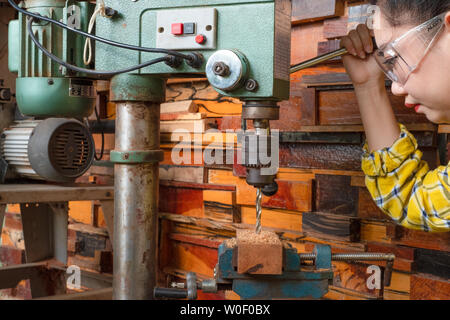 Women standing is craft working drill wood at a work bench with Drill Press power tools at carpenter machine in the workshop Stock Photo