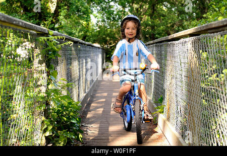 Six-year-old boy cycling on a bridge in the forest Stock Photo