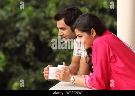 Indian couple leaning against a railing and drinking coffee Stock Photo
