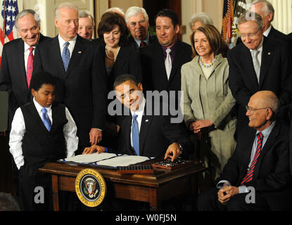U.S. President Barack Obama signs the Health Insurance Reform Bil surrounded by Marcelas Owens (L) of Seattle, Vice President Joe Biden, Vickie Kennedy (behind the president), House Speaker Nancy Pelosi, Senate Majority Leader Harry Reid (R), Rep John Dingell (right, seated) and other congress members in the East Room of the White House in Washington, DC on March 23, 2010.   The historic $938 million health care bill will guaranteed coverage for 32 million uninsured Americans and will touch nearly every American's life.   UPI/Pat Benic Stock Photo